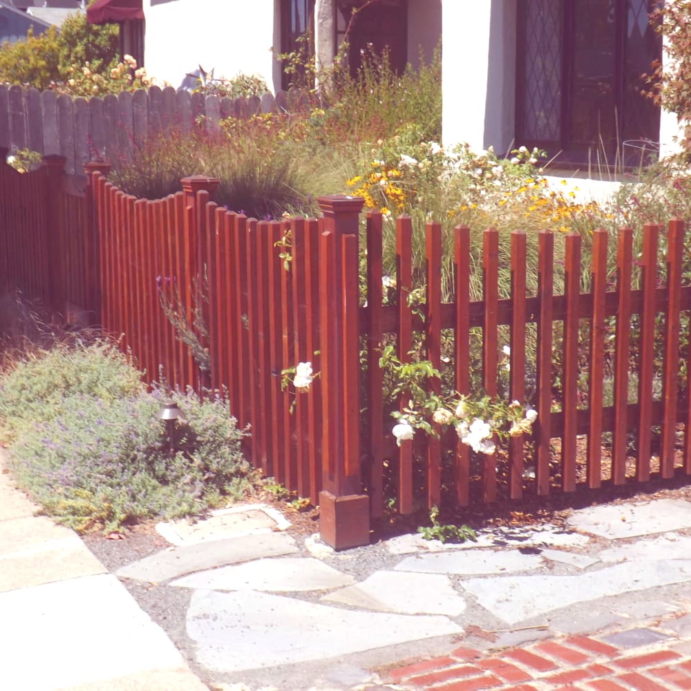 decorative perimeter wood picket fence with maple brown finish protecting garden installation